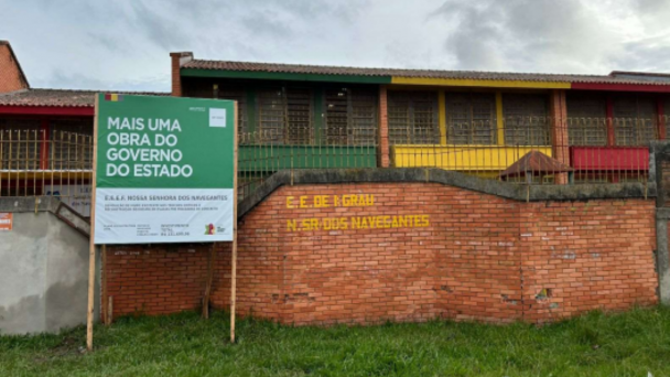 Imagem da fachada da Escola Nossa Senhora dos Navegantes, em Pelotas com um placa indicativa de Mais Uma Obra do Governo do Estado.