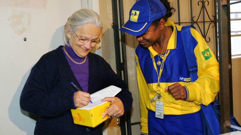 Funcionária dos Correios realiza a primeira entrega do programa Remédio em Casa para Idosos à senhora Jandyra Lopez Souza. A iniciativa, pioneira do governo gaúcho, por meio da Secretaria da Saúde, oferece aos usuários do Sistema Único de Saúde (SUS) com