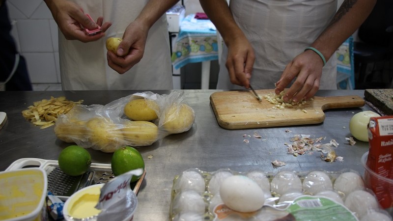 Imagem das mãos de dois jovens diante de uma mesa descascando legumes.