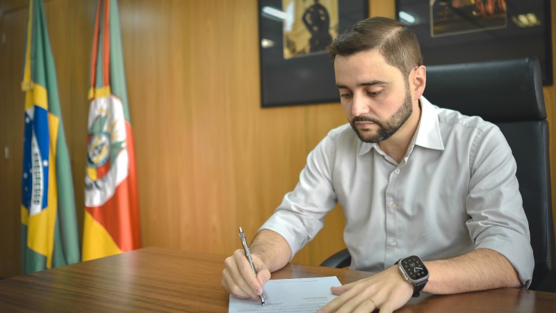 A imagem mostra o governador em exercício Gabriel Souza sentado à sua mesa assinando o decreto de emergência zoosanitária.