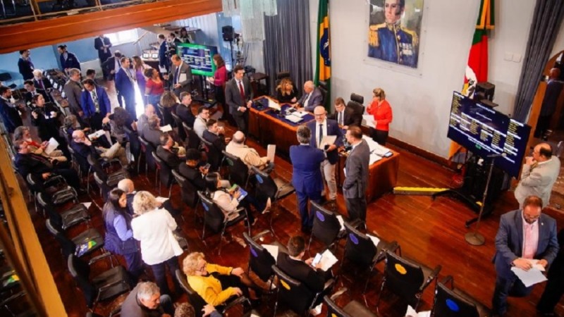 Imagem de cima do Memorial da Assembleia durante a votação do projeto de lei. A foto traduz a movimentação de deputados durante a votação, alguns em pé e outros sentados. Há ainda pequenos grupos em conversa aqui e acolá.