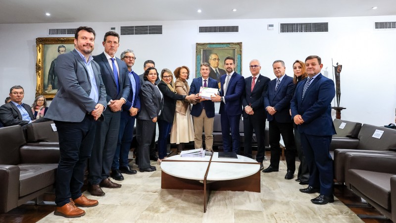 Foto posada do governador e do presidente da Assembleia segurando o documento no centro da imagem, rodeados por diversas pessoas que acompanharam a entrega.