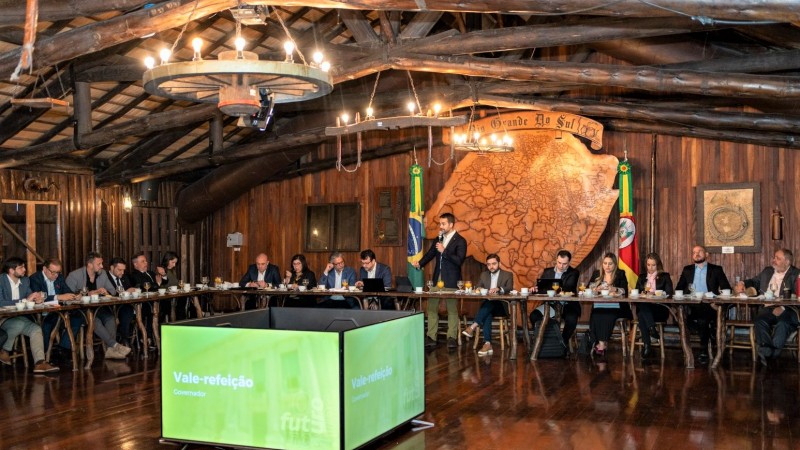 Leite ao centro da imagem com o microfone falando aos deputados que estão sentados a uma mesa que, na imagem, aparece como se fosse em L (éle).