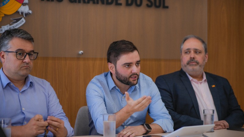 Imagem em close de Gabriel Souza falando e gesticulando durante a reunião. Há um homem do lado direito e outro do lado esquerdo.