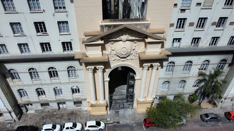 Foto, do alto, da fachada do prédio da Sefaz. Ele é grande e largo, com pórtico. A cor é branca e há muitas janelas.