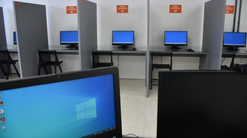 Foto horizontal colorida mostra sala separada em guichês com monitores de computador.