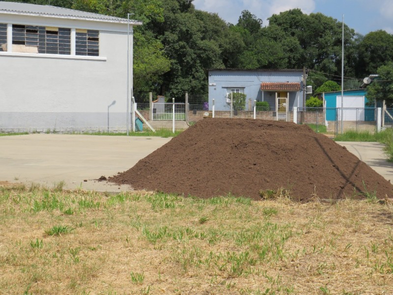Foto em ambiente aberto de um terreno com terra empilhada, dentro de um lote.