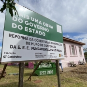 Fachada da Escola Paulo Freire, em Santa Maria, com uma placa de obras do governo do Estado em close.
