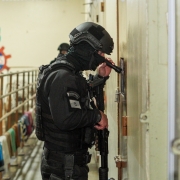 Imagem de um policial de perfil apontando uma lanterna para o interior de uma cela no presídio de Caxias do Sul.