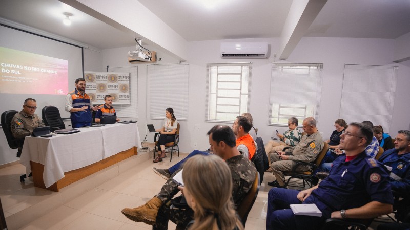 Reunião com o vice em um dos postos avançados no Estado para resolver o problema das chuvas. Em uma mesa à esquerda Gabriel e mais duas pessoas. Mais à direita pessoas sentadas em cadeiras participando da reunião.