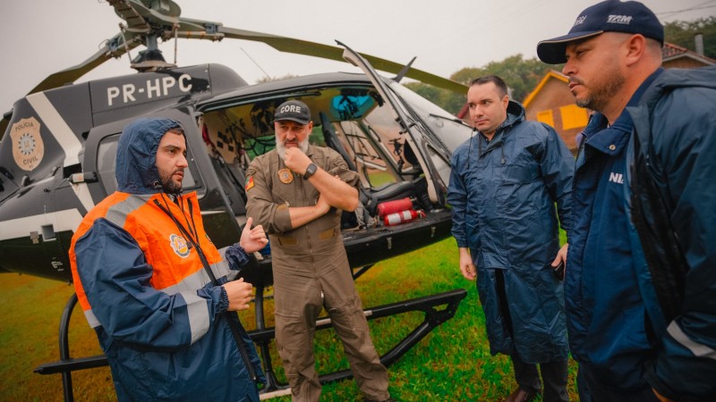Primeiro dia do Gabinete de Crise em Santa Cruz do Sul. Gabriel conversa com outros três homens diante de um helicóptero.