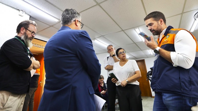 Leite falando ao celular em pé e observado por quatro pessoas. 