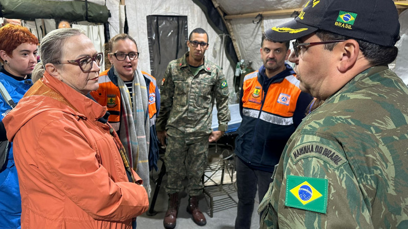 Secretaria da Saúde em Guaíba após enchentes 2024. Arita conversa com um militar no hospital de campanha e é observada por outras quatro pessoas.