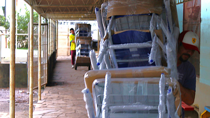 Entrega de mobili&aacute;rio na Escola Guarani. Dois homens em movimento em um dos corredores externos da escola carregando em carrinhos diversas mob&iacute;lias para dentro da escola.