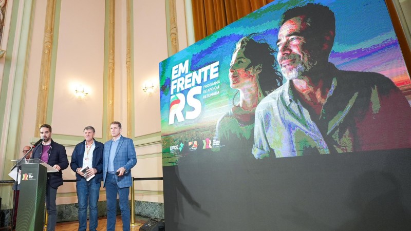 No lançamento do Pronampe Gaúcho, mais à esquerda da imagem, Leite atrás de um púlpito fala em pé ao microfone. Três outros homens aparecem na foto. Mais à direita, uma tela exibe o nome do programa.