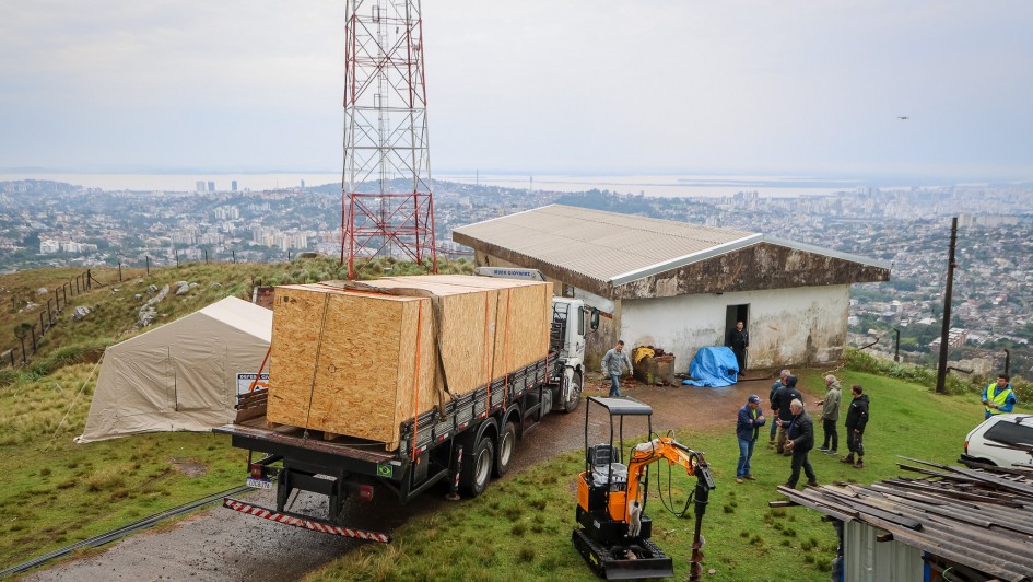 Imagem que mostra a carreta carregando uma enorme caixa onde está o radar chegando ao alto do morro onde o equipamento será instalado.