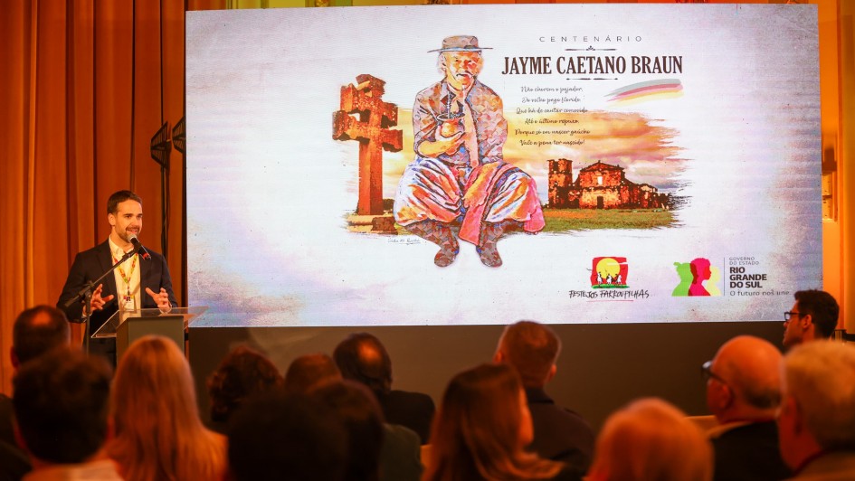 Leite falando ao microfone no lançamento dos Festejos Farroupilhas 2024. Parte da plateia pode ser vista de costas e há uma projeção em uma tela com a imagem de Jayme Caetano Braun, homenageado deste ano.