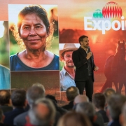 Leite ao microfone e em pé sobre um palco falando Lançamento da Expointer 2024. Parte da platei pode ser vista de costas. Há um grande painel atrás de Leite com imagens de rostos de produtores rurais e onde está escrito 47ª Expointer.