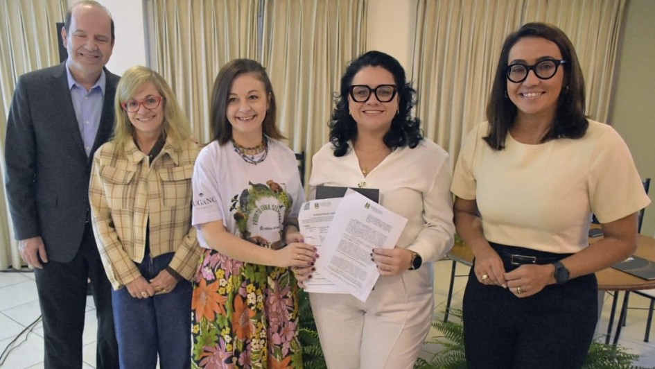 Foto posada com duas pessoas segurando o documento assinado e outras três que participam do ato.