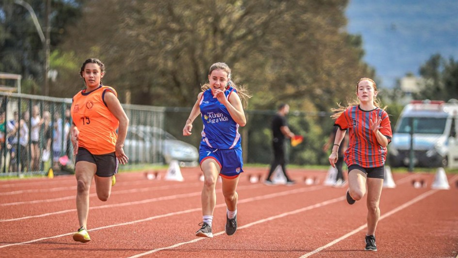 Três atletas jovens competindo em uma pista de atletismo.