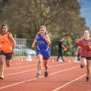 Três atletas jovens competindo em uma pista de atletismo.