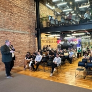 Uma pessoa mais à esquerda falando ao microfone para uma plateia à sua frente. no Meetup Passo Fundo.