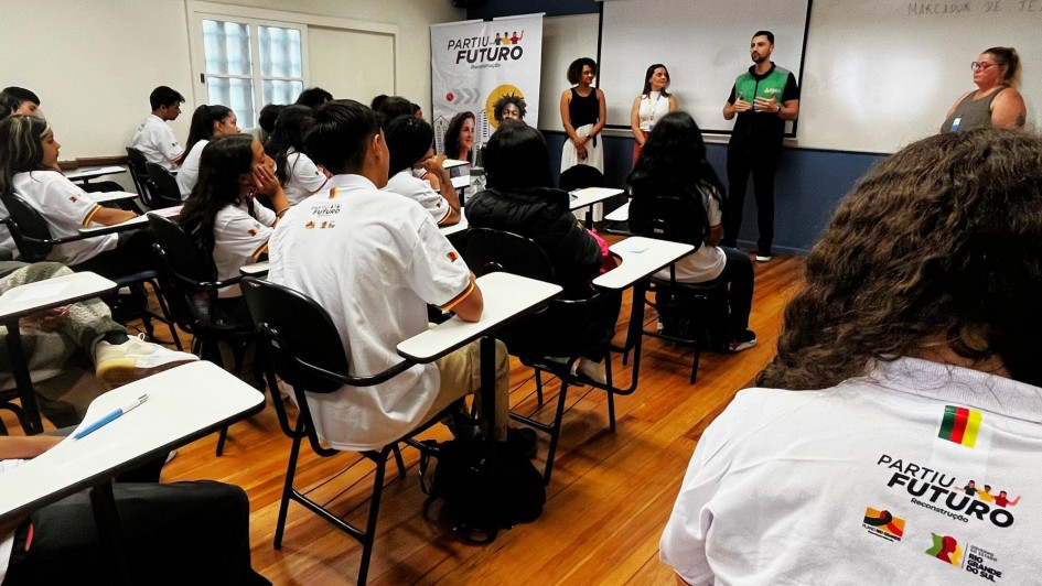 Alunos de costas em uma sala de aula com quatro pessoas falando com eles na parte da frente da sala de aula.