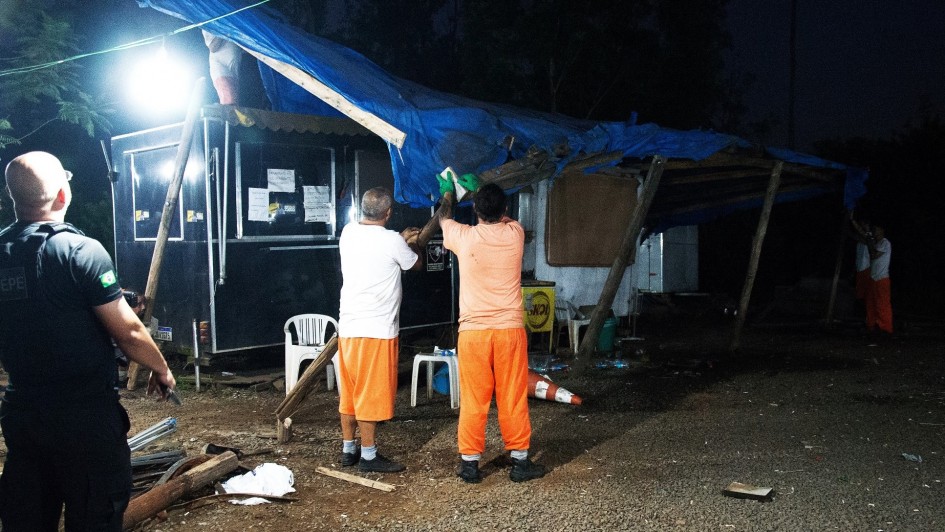 Imagem de policial e de servidores desmontando tendas com cobertura de lona.