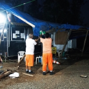 Imagem de policial e de servidores desmontando tendas com cobertura de lona.