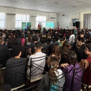 Encerramento das palestras Sapiência e Enrolado de 2024. Um enorme auditório lotado de crianças e adolescentes vistos de costas e a palestrante mais ao fundo.