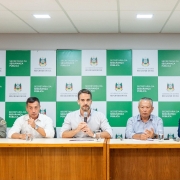 Leite e mais quatro homens sentados atrás de uma bancada para a coletiva. Leite segura o microfone e fala com os jornalistas.