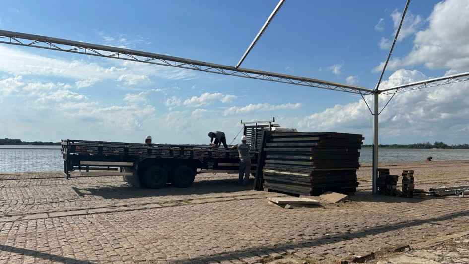 Imagem externa da montagem de um palco. com trabalhadores empilhando peças de metal abaixo de uma estrutura de metal