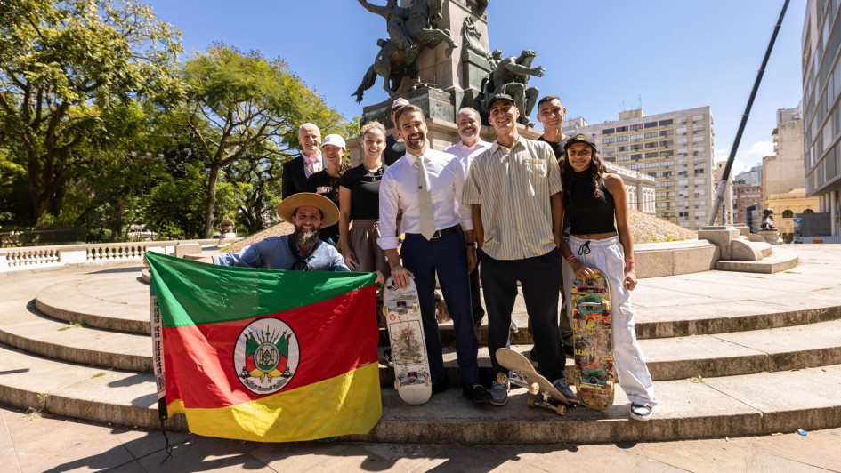 Foto posada de Leite com skatistas na Praça Matriz, em Porto Alegre. O secretário do Esporte e Lazer, segura uma bandeira do Rio Grande do Sul aberta.