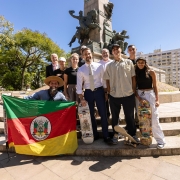 Foto posada de Leite com skatistas na Praça Matriz, em Porto Alegre. O secretário do Esporte e Lazer, segura uma bandeira do Rio Grande do Sul aberta.