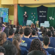 Imagem de uma pessoa em cima do palco falando para a plateia, que pode ser vista de costas.