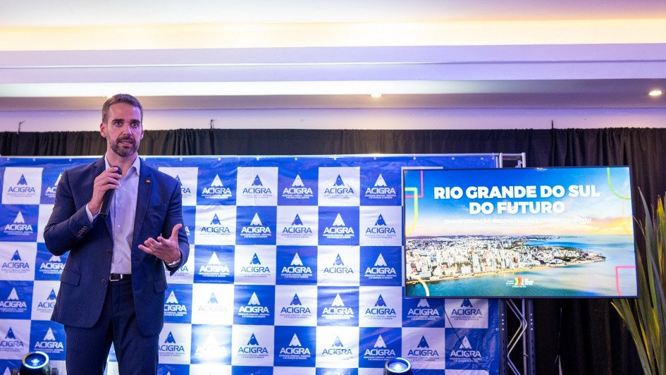 Governador aparece de terno, em pé, falando ao microfone. Ao fundo, um painel com a logo da Acigra em azul e branco e uma tela em que aparece "Rio Grande do Sul do Futuro"