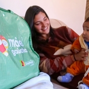 Imagem de uma mãe com um bebê no colo ao lado de uma bolsa do kit Mãe Gaúcha.