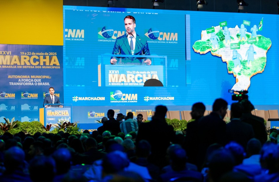 Leite falando a atrás de um púlpito, sobre o palco, na marcha dos municípios em Brasília 2025. Parte da plateia pode ser vista de costas.