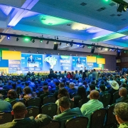 Imagem geral de Leite falando ao longe, no palco, para a enorme plateia, vista de costas, na marcha dos municípios em Brasília 2025.