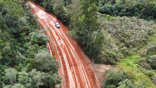 Foto de estrada de terra cortando uma mata. Um carro passa por ela.