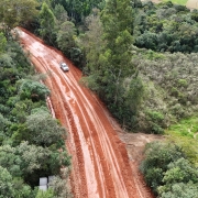 Foto de estrada de terra cortando uma mata. Um carro passa por ela.