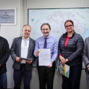 Foto posada com participantes do ato em pé, de frente, exibindo o documento assinado. 