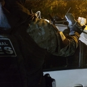 Imagem mostra policial com coleta da Polícia Penal Gaes segurando drone com a mão direita, sobre um veículo de cor branco