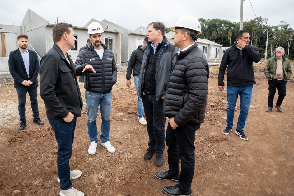 Imagem mostra governador Eduardo Leite e outras pessoas conversando em área onde ao fundo aparecem casas que estão sendo construídas