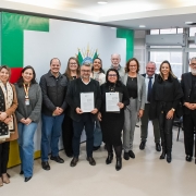 Foto posada de diversas pessoas reunidas em torno de duas delas que seguram os documentos recém assinados.