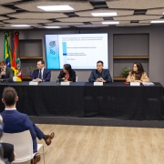 Foto da mesa com cinco pessoas concedendo entrevista coletiva sobre descontos em folha de pagamento de servidores inativos. Duas pessoas da plateia podem ser vistas de costas.