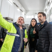 A imagem mostra uma visita a uma casa de bombeamento de água. À direita está o governador Eduardo Leite, de casaco preto, observando atentamente enquanto um homem com casaco amarelo com faixas refletivas aponta algo fora da imagem. Ao centro, uma mulher com casaco preto acompanha a cena.
