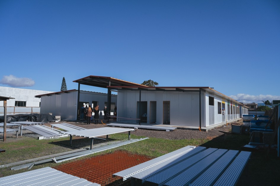 A imagem mostra o vice-governador Gabriel Souza vistoriando uma obra em uma escola. Ele está acompanhado por outras pessoas no canteiro de construção, onde estruturas metálicas e painéis indicam o uso de construção a seco. O cenário transmite um momento de inspeção e avanço em melhorias na infraestrutura educacional.