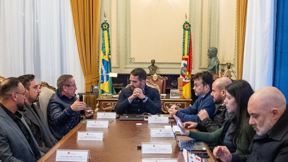 A imagem mostra uma reunião formal entre o governador Eduardo Leite e o prefeito de Canoas, Airton Souza, no Palácio Piratini. O encontro ocorreu em um ambiente institucional, com bandeiras oficiais e decoração clássica, e teve como foco o avanço na liberação de cerca de R$ 200 milhões para obras de contenção de cheias no município. A cena transmite um momento de diálogo técnico e político voltado à reconstrução e prevenção de desastres.