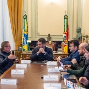 A imagem mostra uma reunião formal entre o governador Eduardo Leite e o prefeito de Canoas, Airton Souza, no Palácio Piratini. O encontro ocorreu em um ambiente institucional, com bandeiras oficiais e decoração clássica, e teve como foco o avanço na liberação de cerca de R$ 200 milhões para obras de contenção de cheias no município. A cena transmite um momento de diálogo técnico e político voltado à reconstrução e prevenção de desastres.